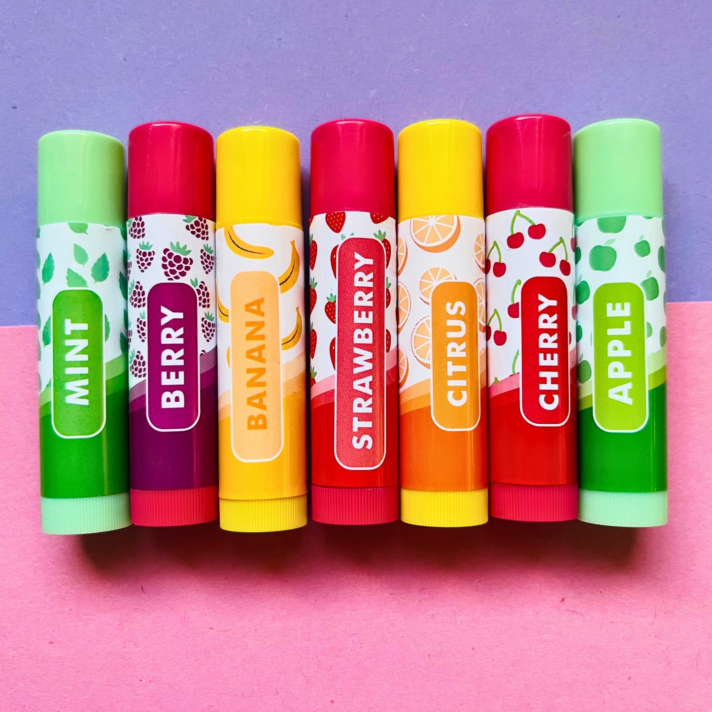 Shot of all lip balm flavours available: Mint, Berry, Banana, Strawberry, Citrus, Cherry and Apple