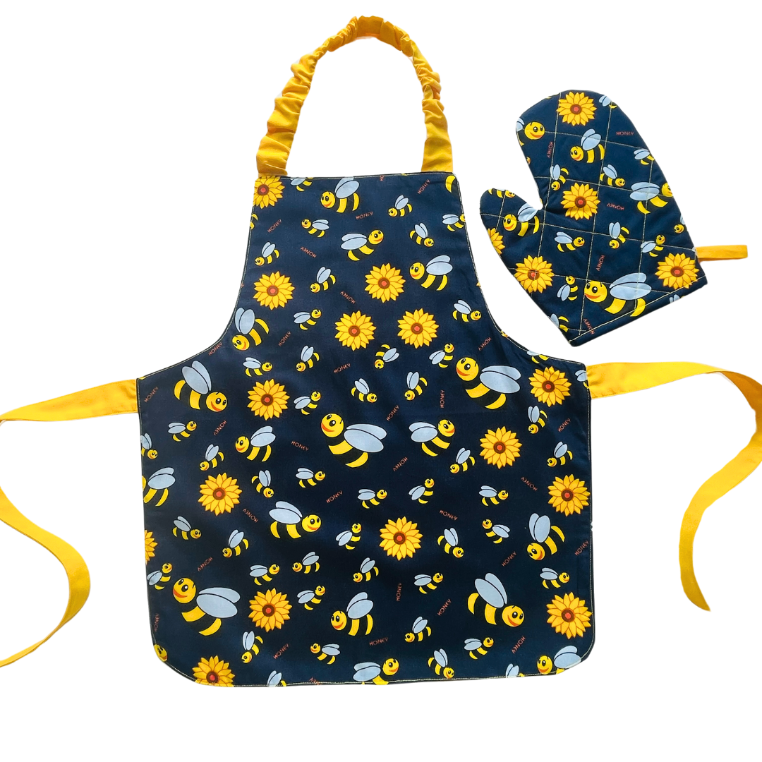 A child’s apron and matching oven mitt set. Pattern is navy and yellow with cartoon bumble bees and yellow flowers all over.