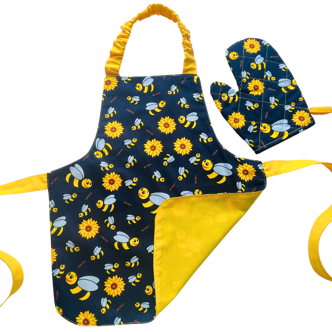 A child’s apron and matching oven mitt set. Pattern is navy and yellow with cartoon bumble bees and yellow flowers all over.