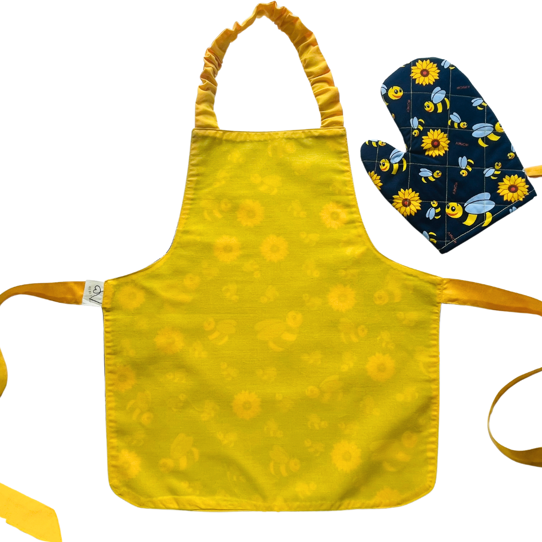 A child’s apron and matching oven mitt set. Pattern is navy and yellow with cartoon bumble bees and yellow flowers all over.
