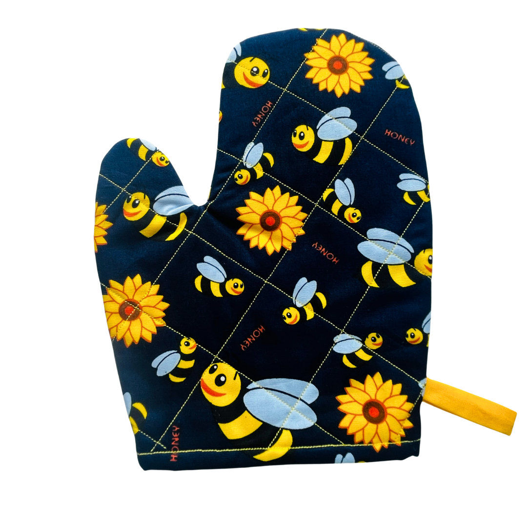 A child’s apron and matching oven mitt set. Pattern is navy and yellow with cartoon bumble bees and yellow flowers all over.