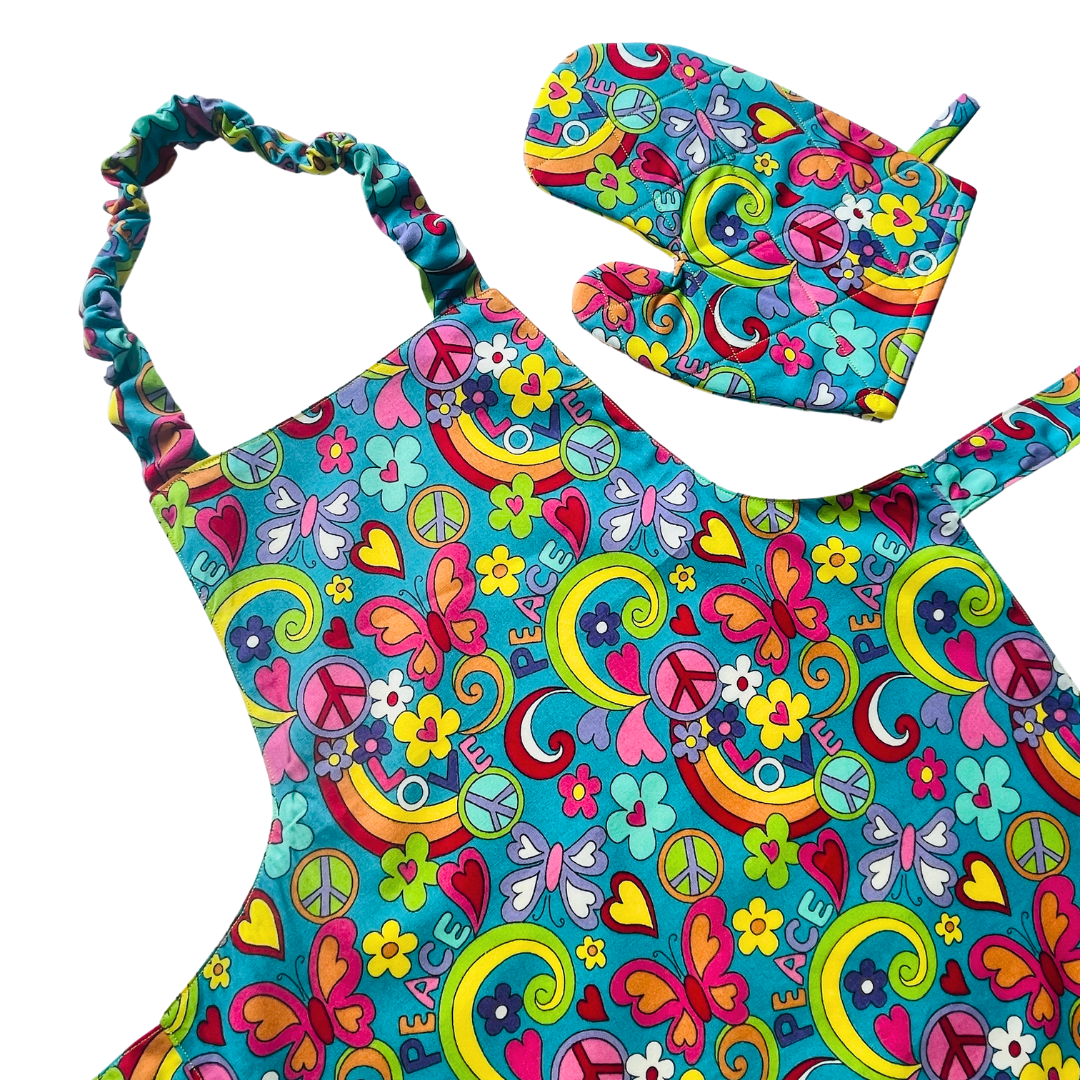 A child’s apron and matching oven mitt set. Pattern is turquoise with brightly coloured 60s inspired funky pictures all over.