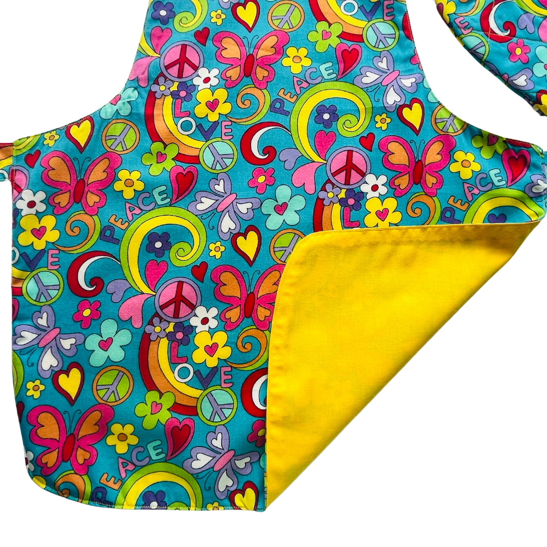 A child’s apron and matching oven mitt set. Pattern is turquoise with brightly coloured 60s inspired funky pictures all over.