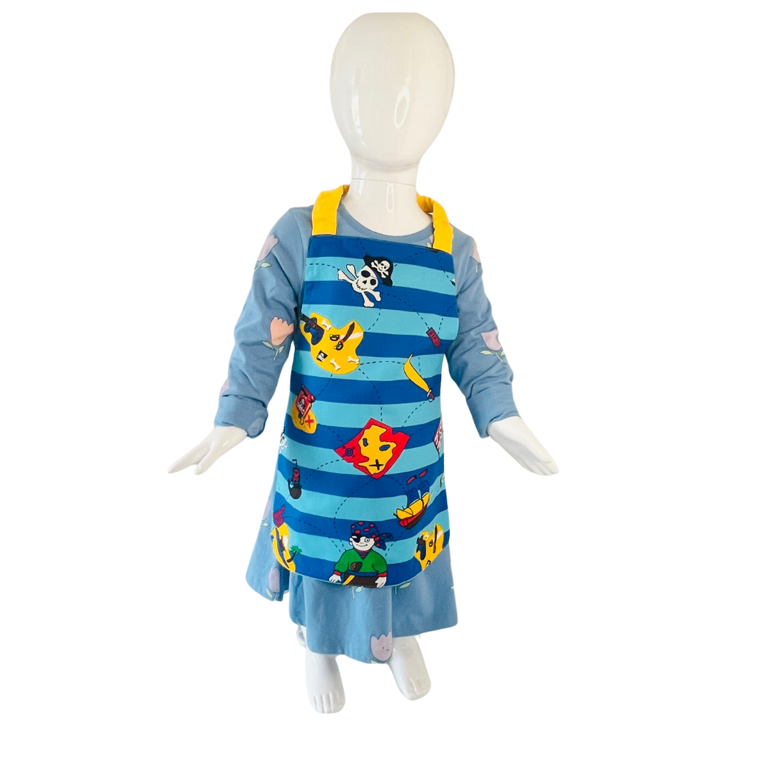 A child’s apron and matching oven mitt set. Pattern is light and dark blue with yellow and has pirate pictures such as treasure, maps and ships all over. Styled on mannequin.