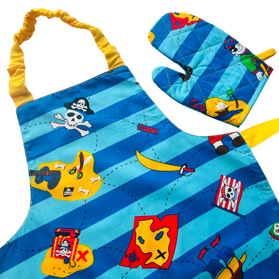 A child’s apron and matching oven mitt set. Pattern is light and dark blue with yellow and has pirate pictures such as treasure, maps and ships all over.