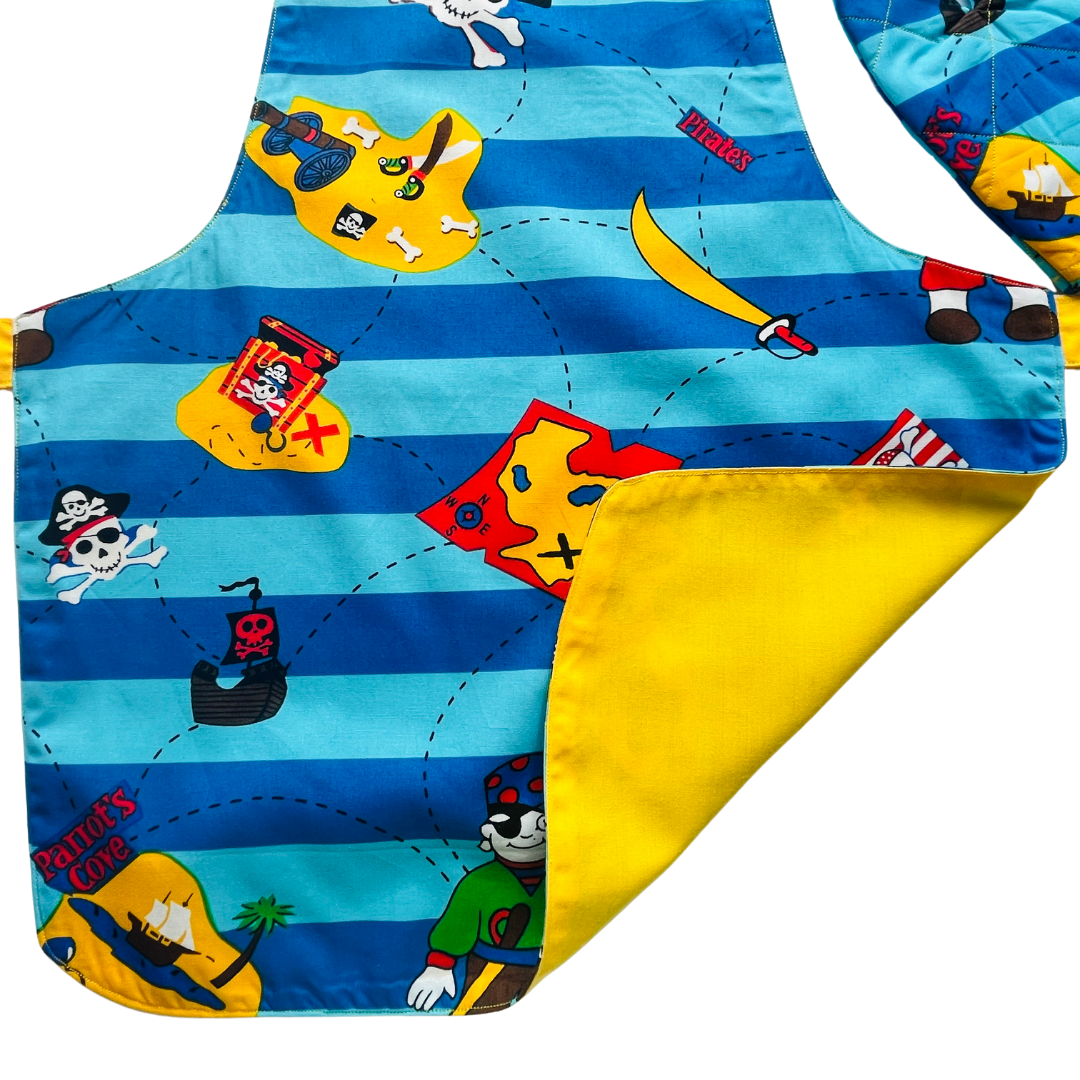 A child’s apron and matching oven mitt set. Pattern is light and dark blue with yellow and has pirate pictures such as treasure, maps and ships all over.