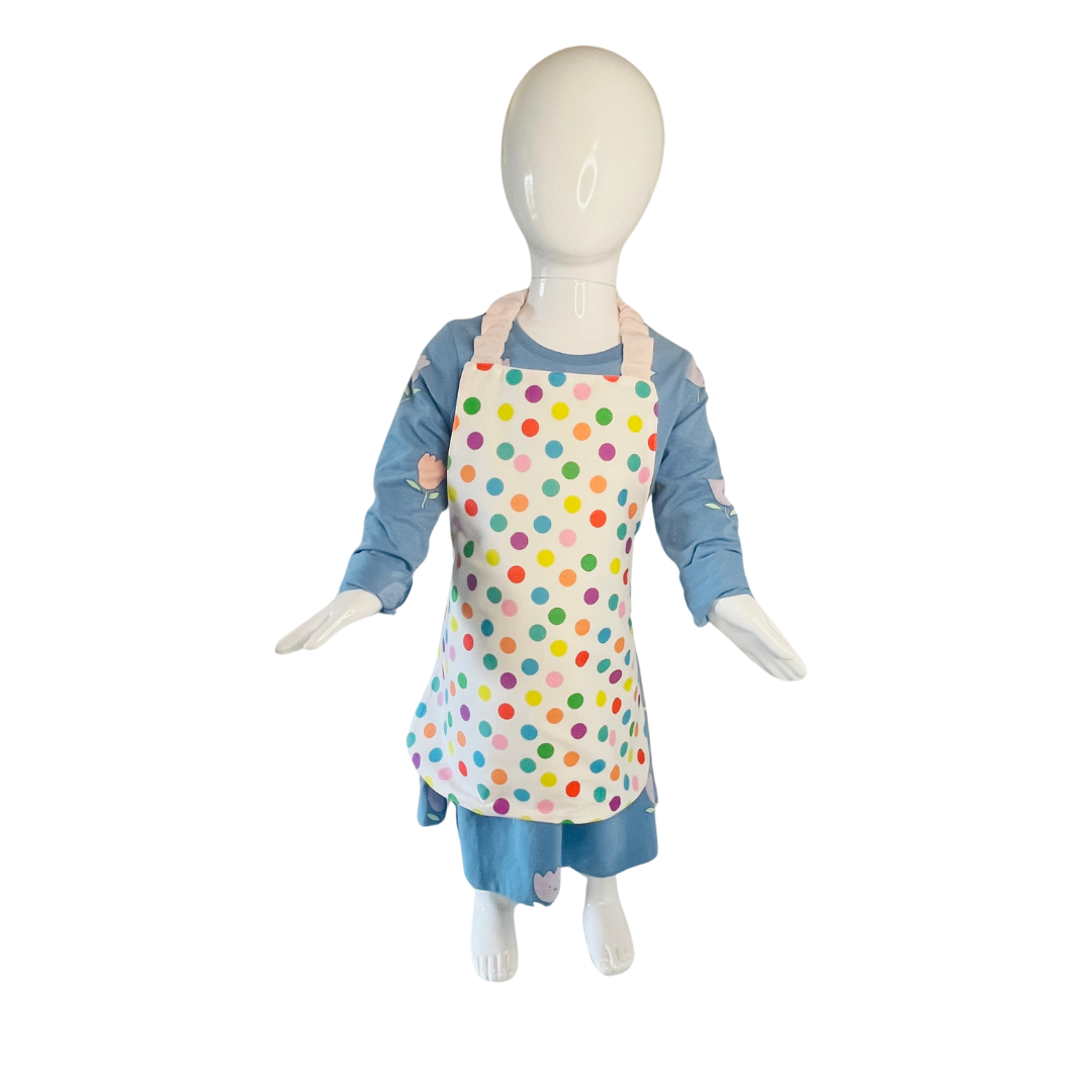 A child’s apron and matching oven mitt set. Pattern is white and pale pink and has multicoloured spots all over. Styled on mannequin.