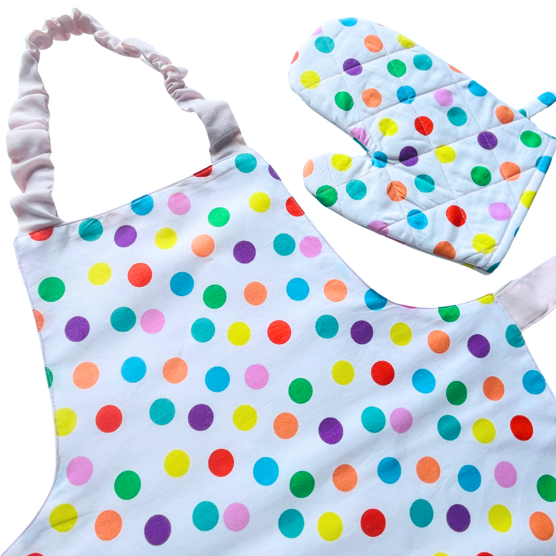 A child’s apron and matching oven mitt set. Pattern is white and pale pink and has multicoloured spots all over.